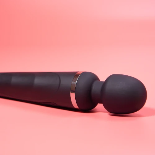 На данном изображении показан черный вибромассажер на розовом фоне.