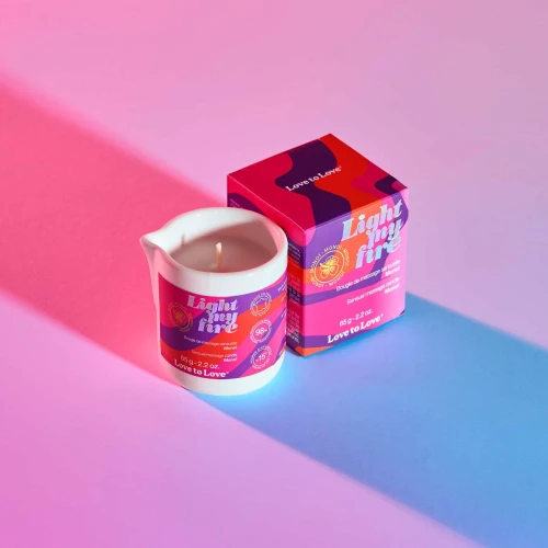 На фото изображена белая свеча для массажа Love To Love LIGHT MY FIRE Monoi (65 мл) для пар на разноцветном фоне.