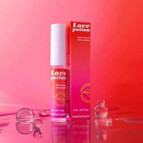 На фото зображено рожевий стимулюючий блиск для губ Love To Love Love Potion - Gloss Sensuel 8 мл унісекс на різнокольоровому фоні.