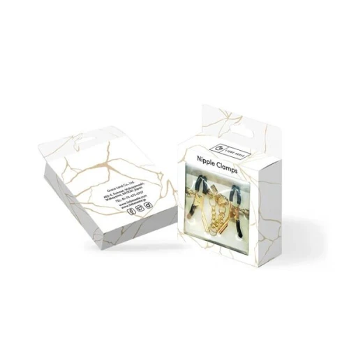 На фото зображено чорно-золоті затискачі для сосків з ланцюжком Feral Feelings - Clover nipple clamps у темній коробці для жінок на білому тлі