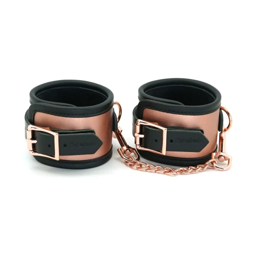 На фото зображені чорні поножі із рожевим золотом Liebe Seele Rose Gold Memory Ankle Cuffs на білому тлі