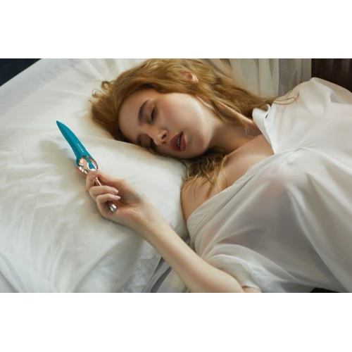 На фото дівчина на білому постелі з вібратором в руці