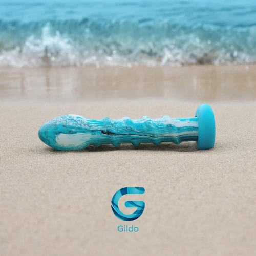 На фото зображено скляне дилдо морського кольору Gildo Ocean Wave Glass Dildo унісекс на тлі пляжу.