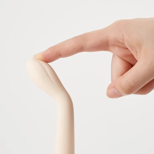 На фото: бежевий вібратор, який торкає палець.