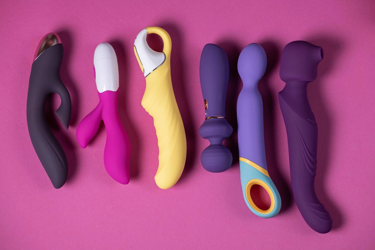 на розовом фоне изображены большие вибраторы из сексшоп разных цветов