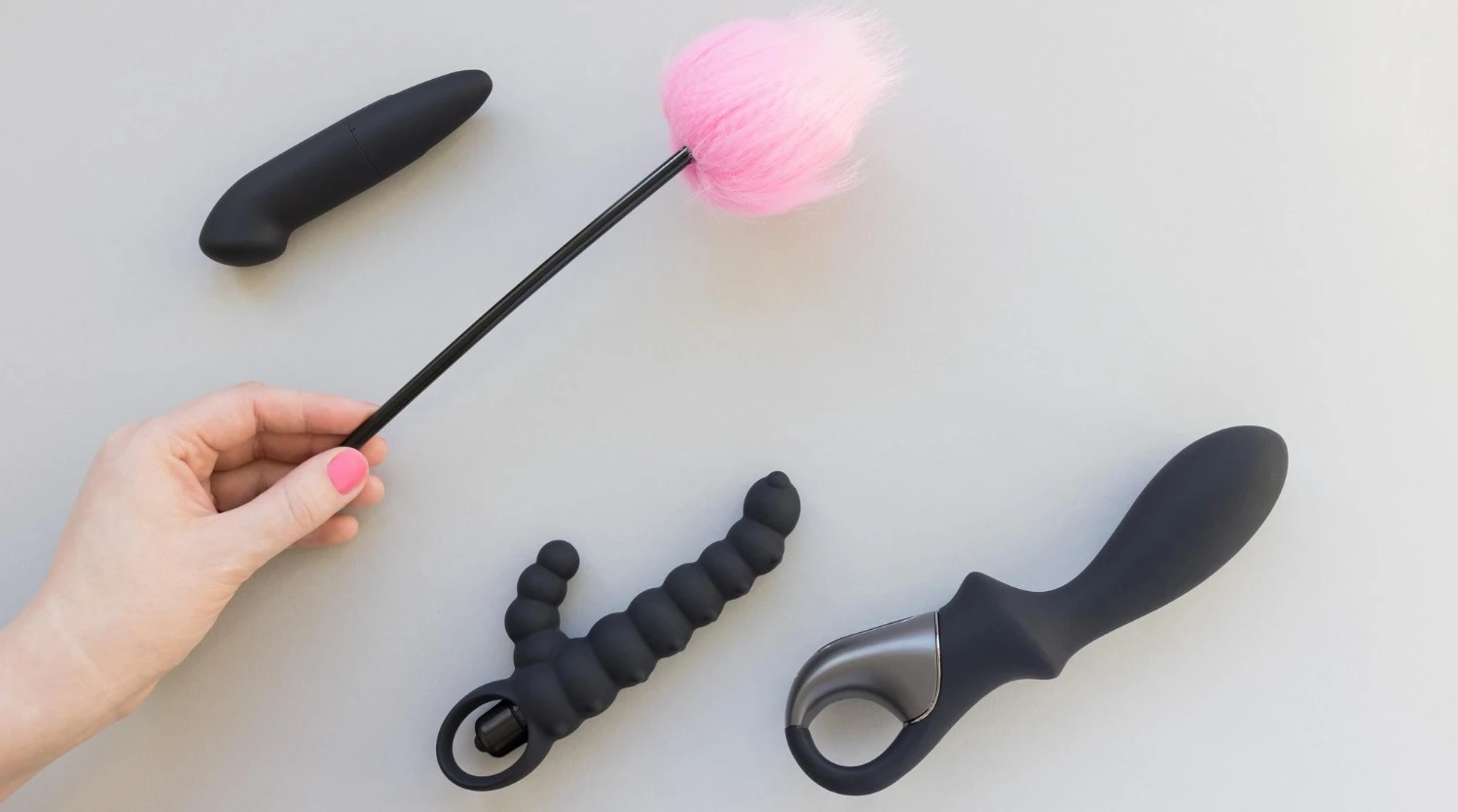 на сером фоне изображены вибрирующая черная анальная пробка, черный анальный вибратор и пушок для секса