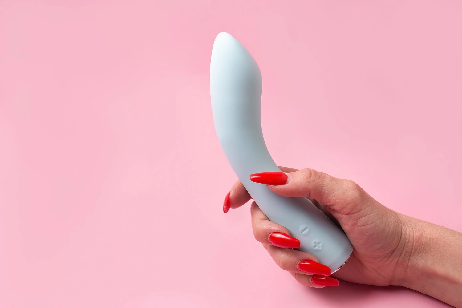 на фото на рожевому фоні зображений бірюзовий вібратор в жіночій руці