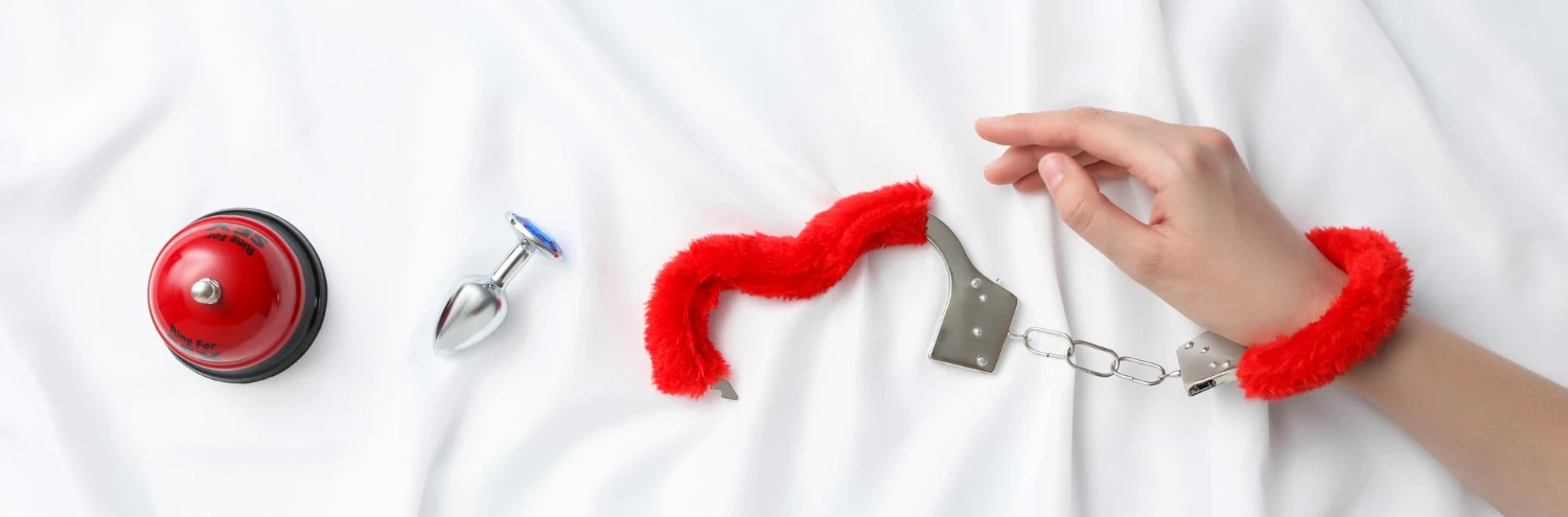 на білій простині зображені черврні наручники для БДСМ, анальна металева пробка