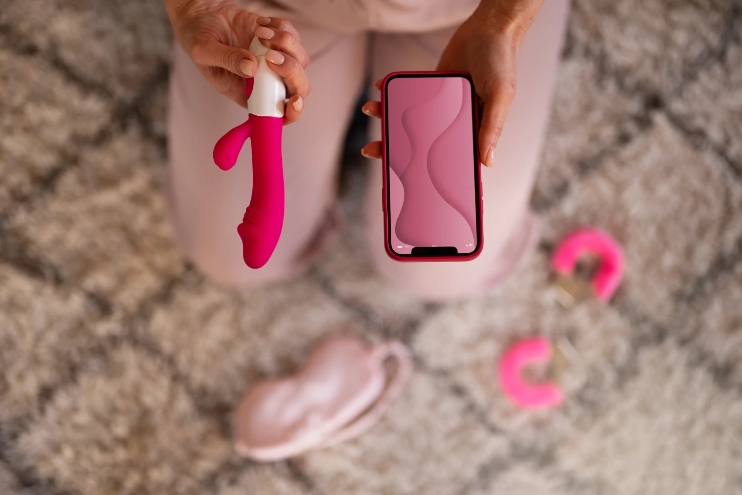 на фото зображений вібратор з керуванням з телефону рожевого кольору в руках жінки