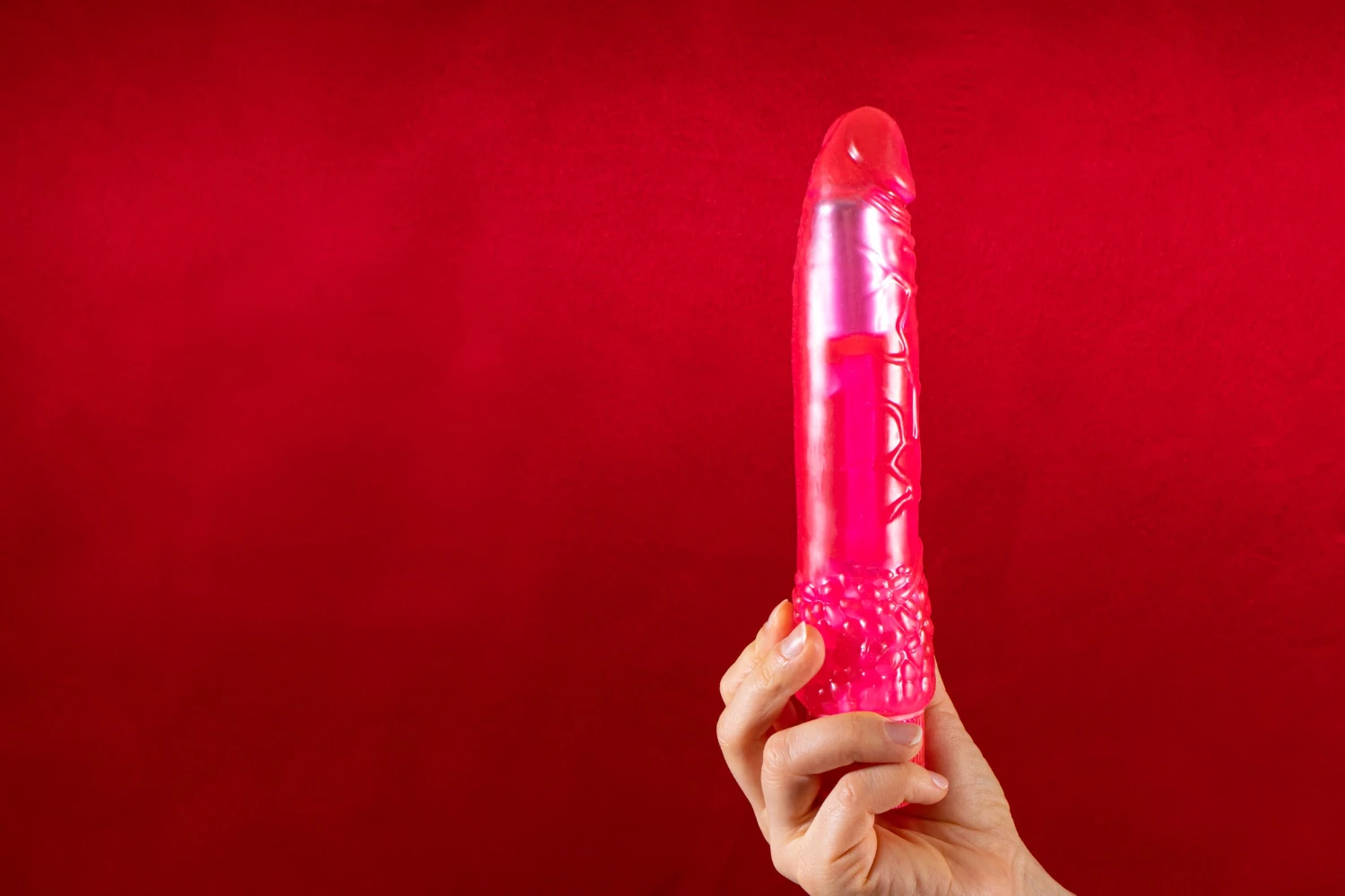 на красном фоне изображен розовый дилдо резиновый в женских руках