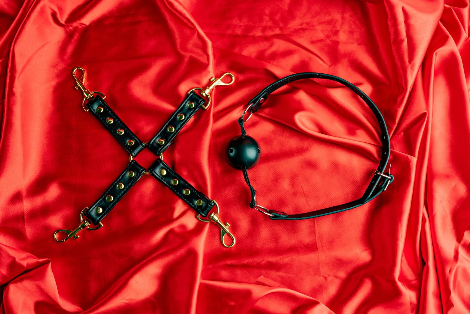 на червоному шовкому простирадлі чорний кляп для БДСМ та фіксатори