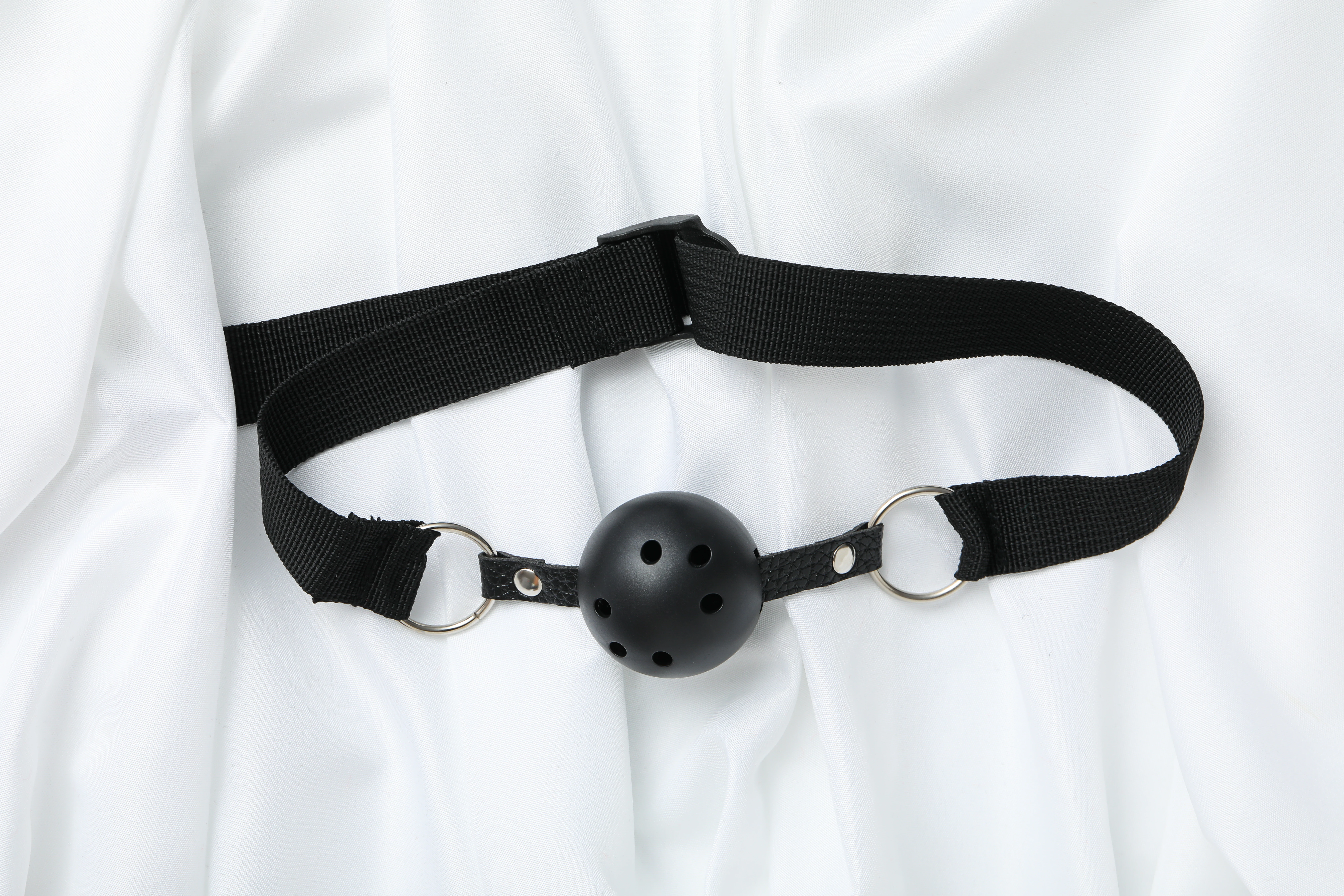 на белой простыне изображен черный кляп шарик для БДСМ