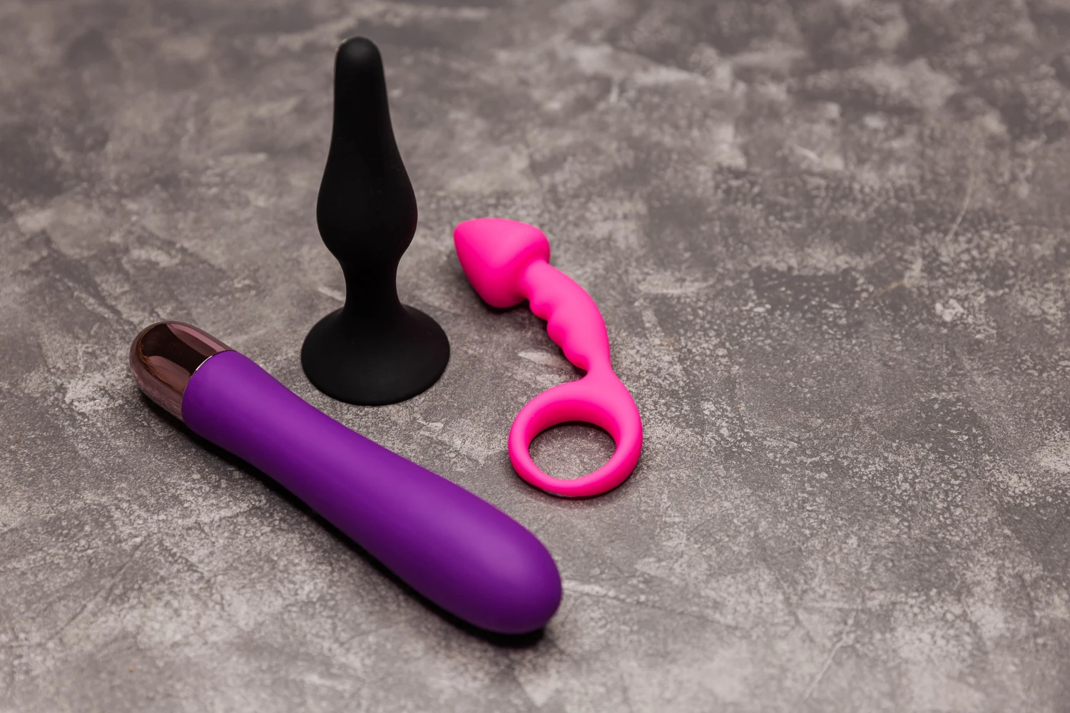 на кам'яному столі лежать чорна та рожева анальні втулки та анальний вібратор