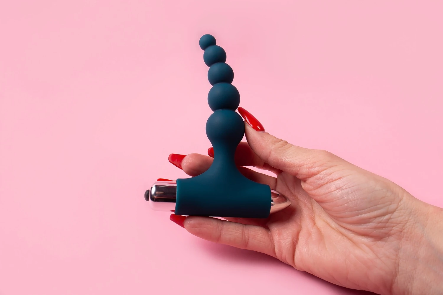 анальна вібропробка унісекс силіконова в жіночій руці з червоними ногтями на рожевому фоні
