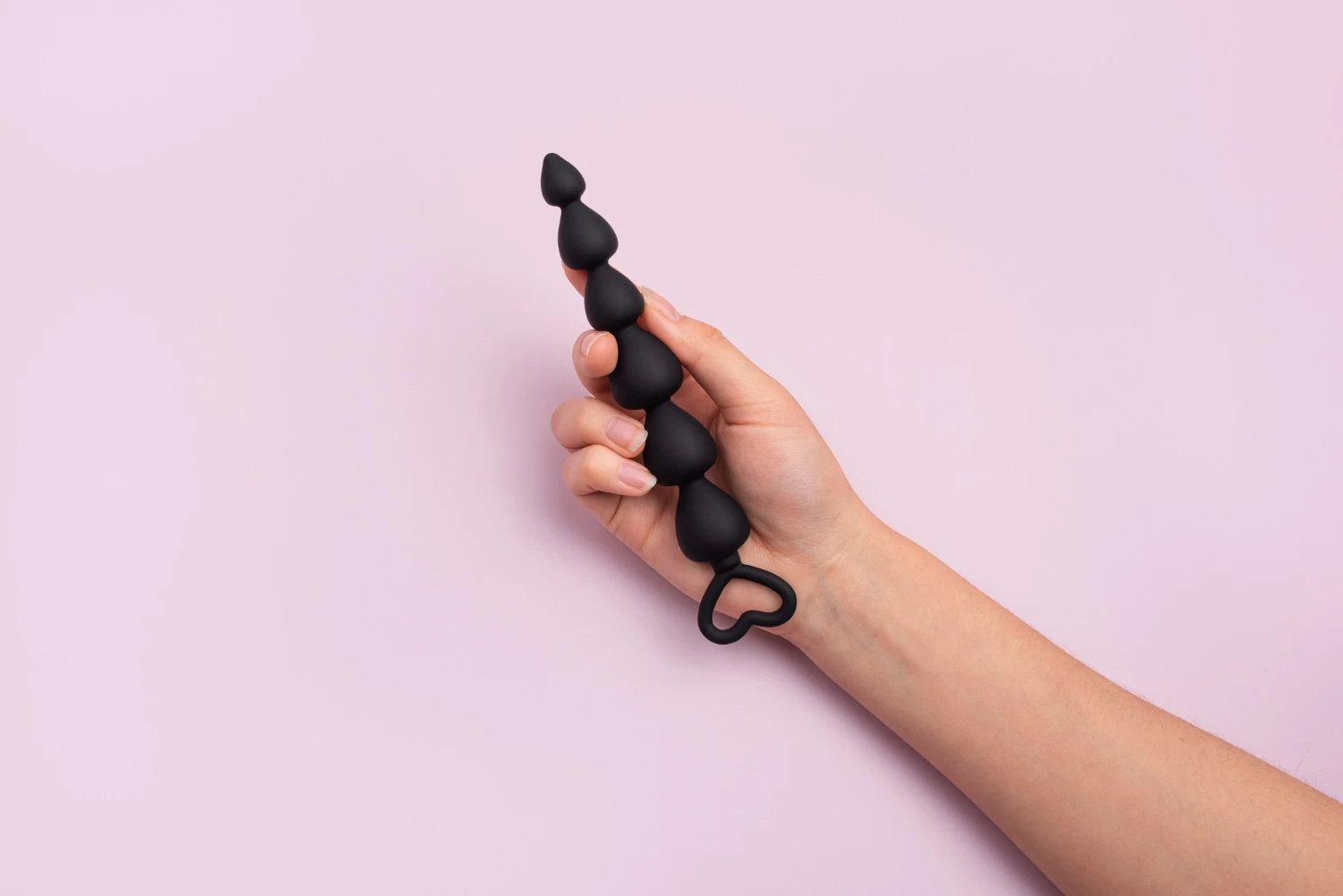 черная силиконовая анальная цепочка в женских руках на розовом фоне