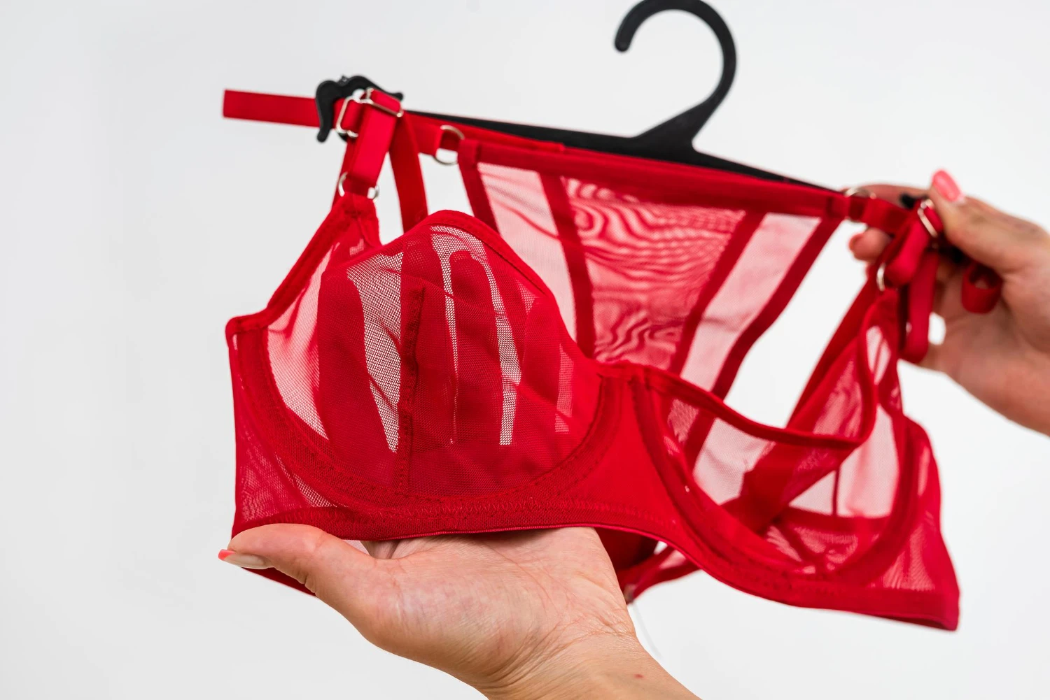 на фото изображен сексуальный красный комплект нижнего белья для женщин на тремпеле в женских руках