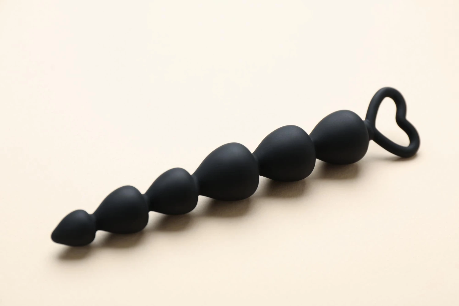 на бежевом фоне изображены черные анальные бусы силиконовые для попы
