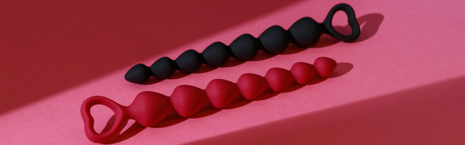 на рожевому фоні анальні буси чорного та червого кольорів із силикону