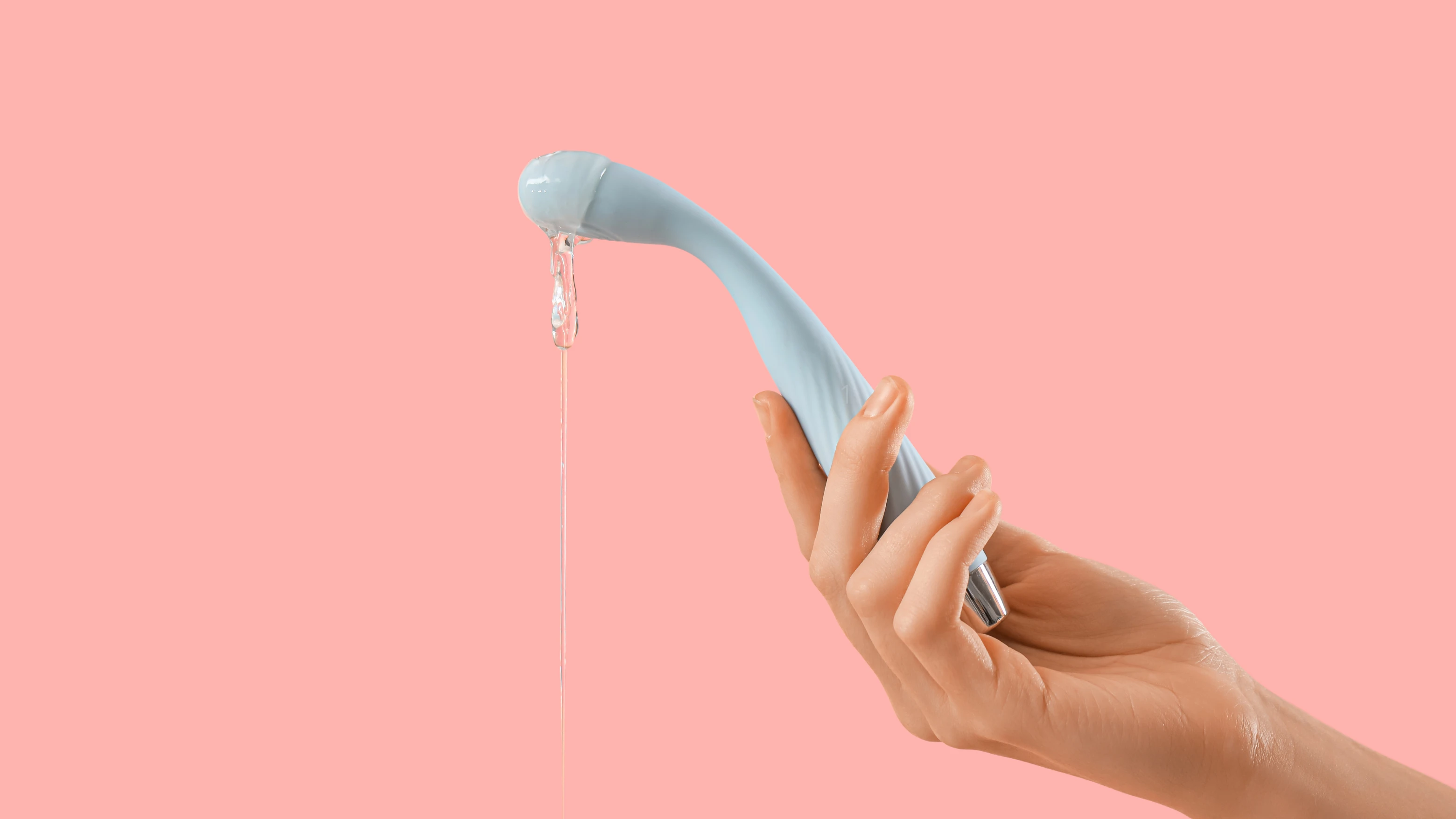 на персиковому фоні зображений реалістичний вібратор бірюзового кольору з лубрікантом