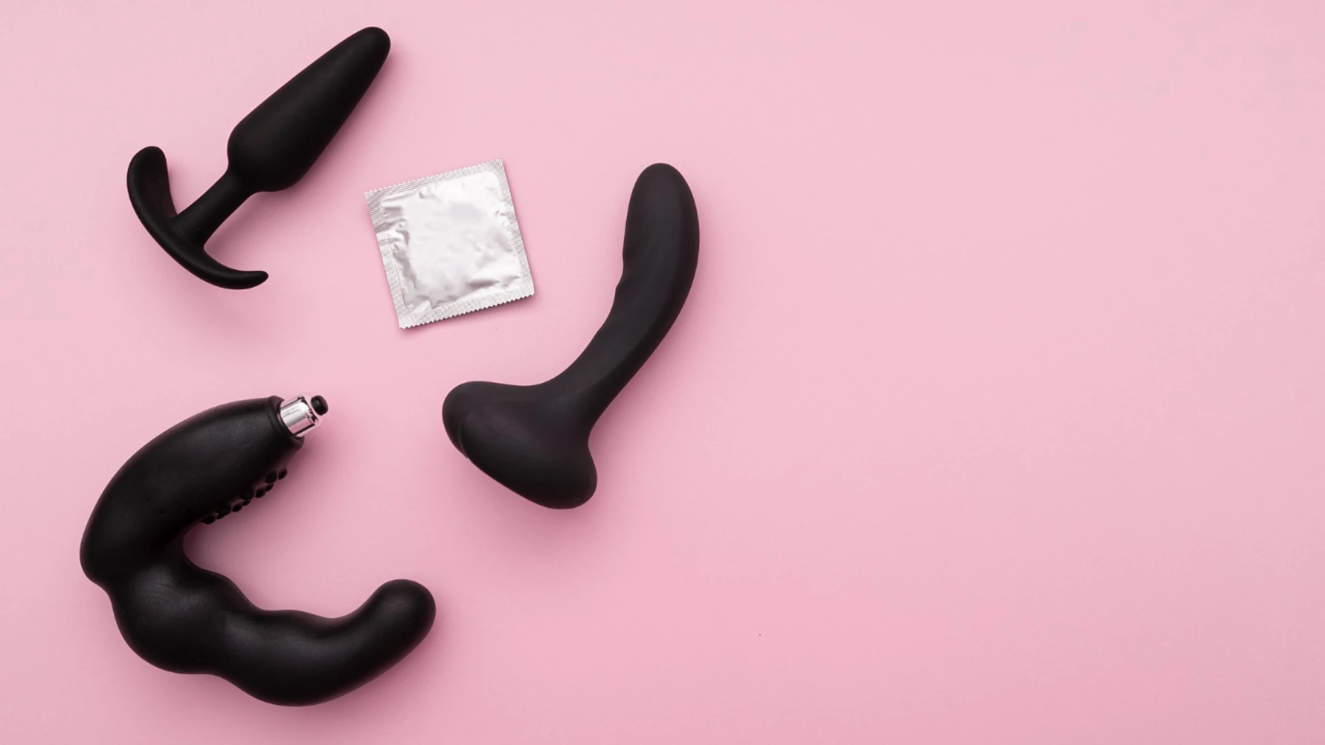 на розовом фоне изображены большие черные анальные пробки для секса и презерватив