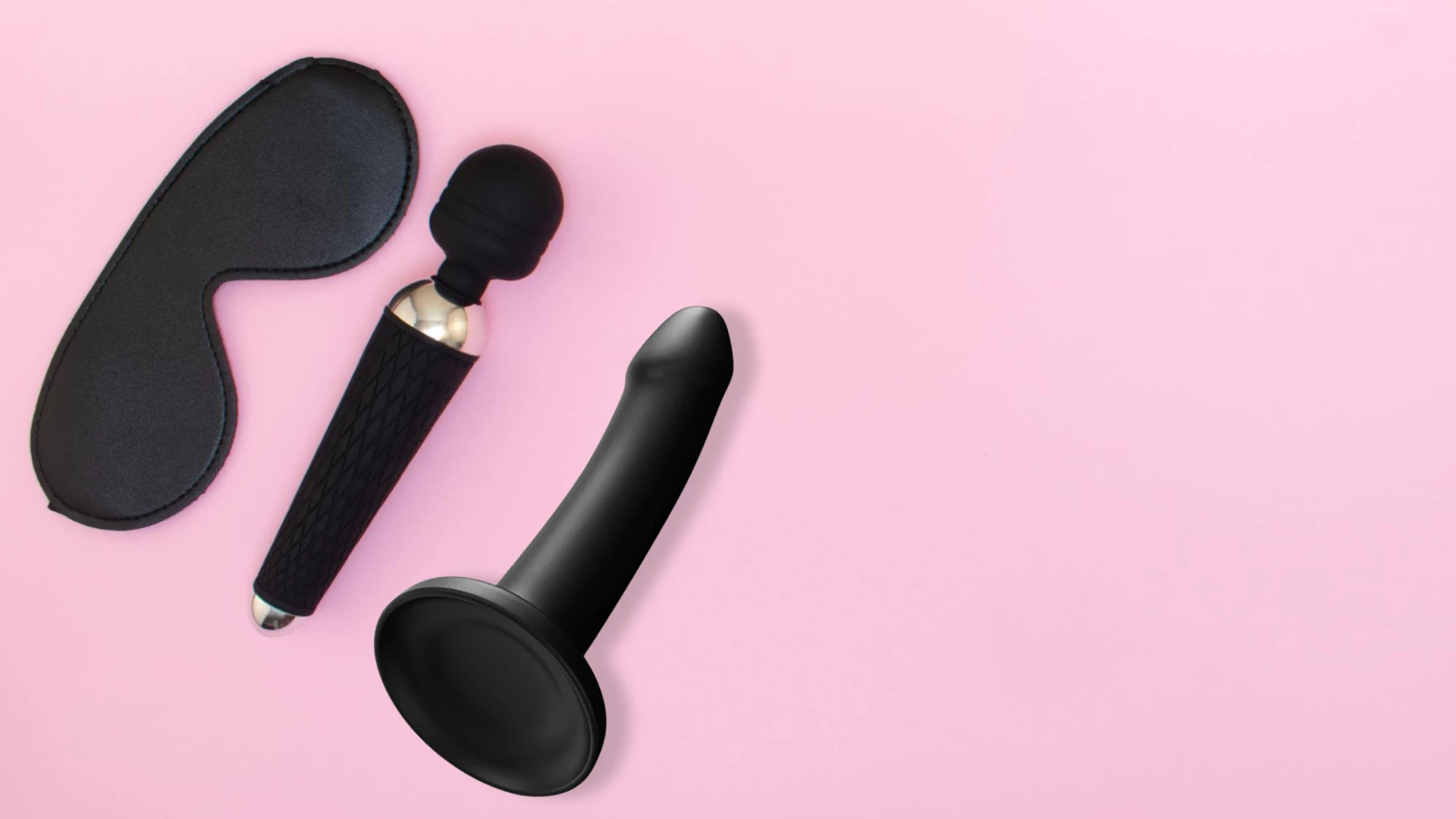 на рожевому фоні чорний ділдо, чорний фаллоімітатор мікрофон та чорна маска для сексу