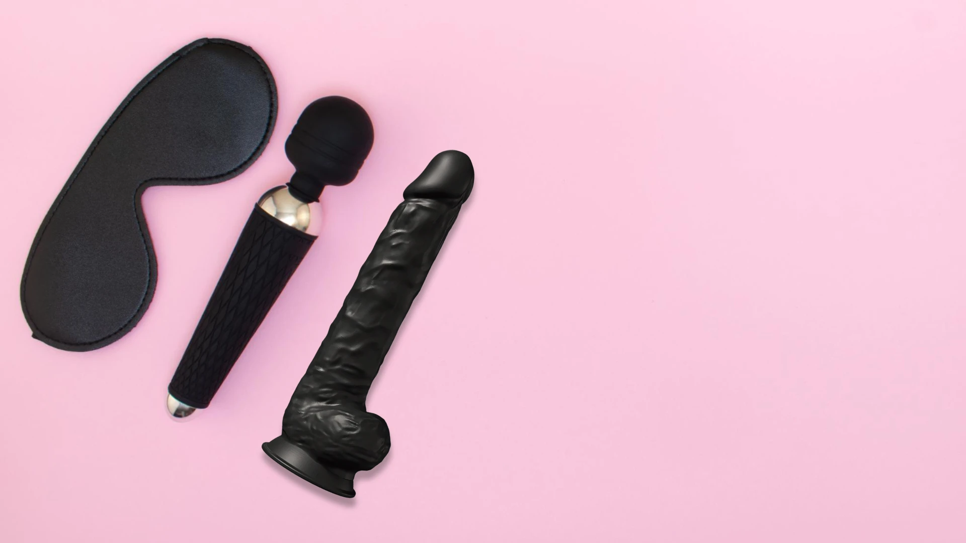 на розовом фоне изображен черный дилдо, черный вибратор и маска для секса черная