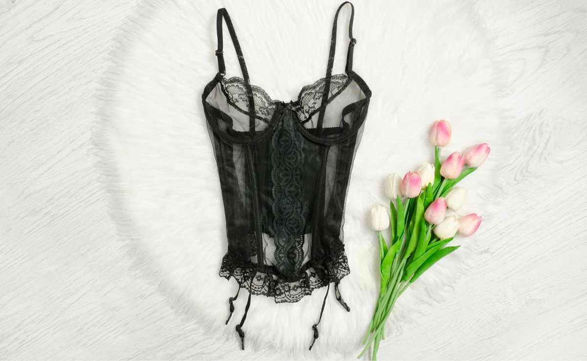 чорний еротичний корзет лежить на білій ковдрі поряд з тюльпанами