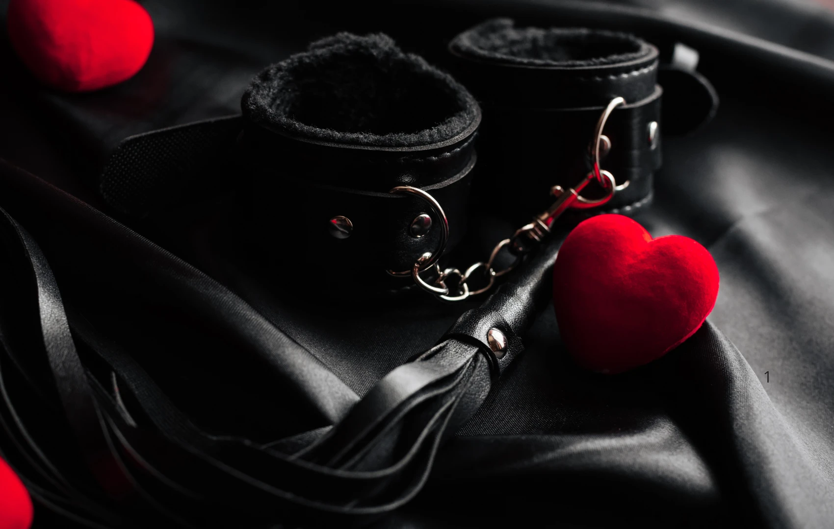 на чорному шовку зображені чорні наручники для БДСМ м'які, пльотка та маленьке черноне сердце