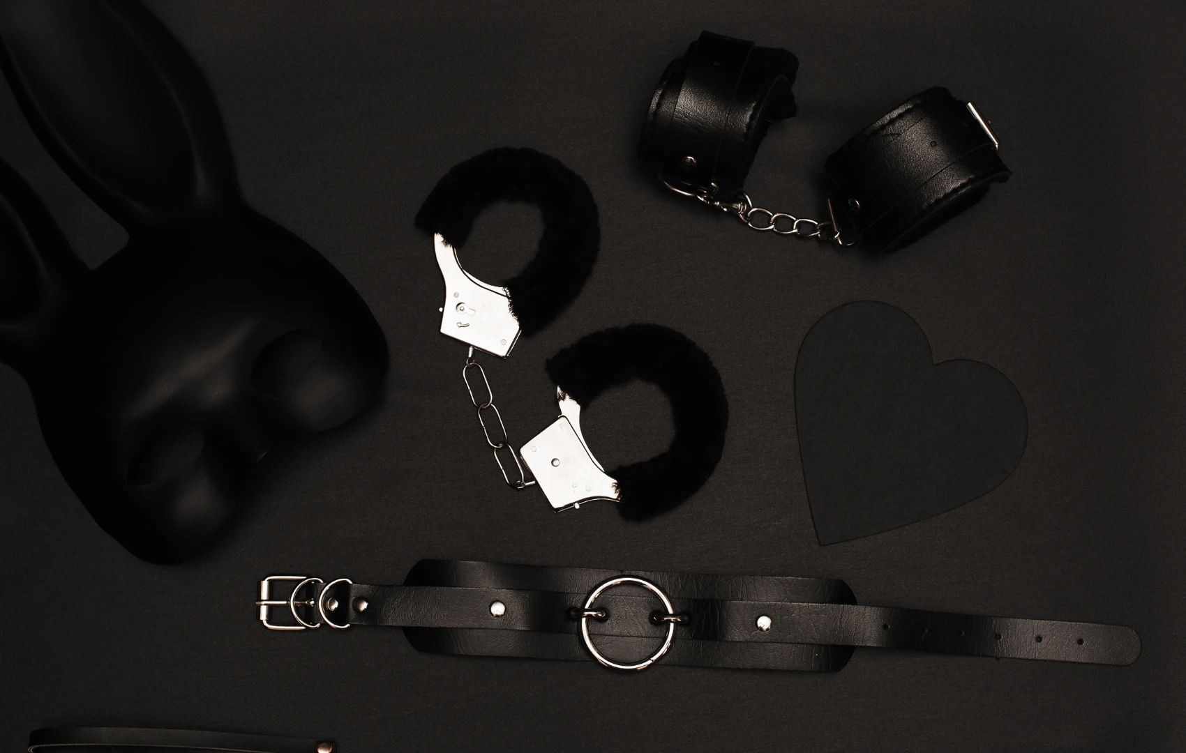 на чорному фоні зображені два види наручників для сексу і інші чорні атрибути БДСМ