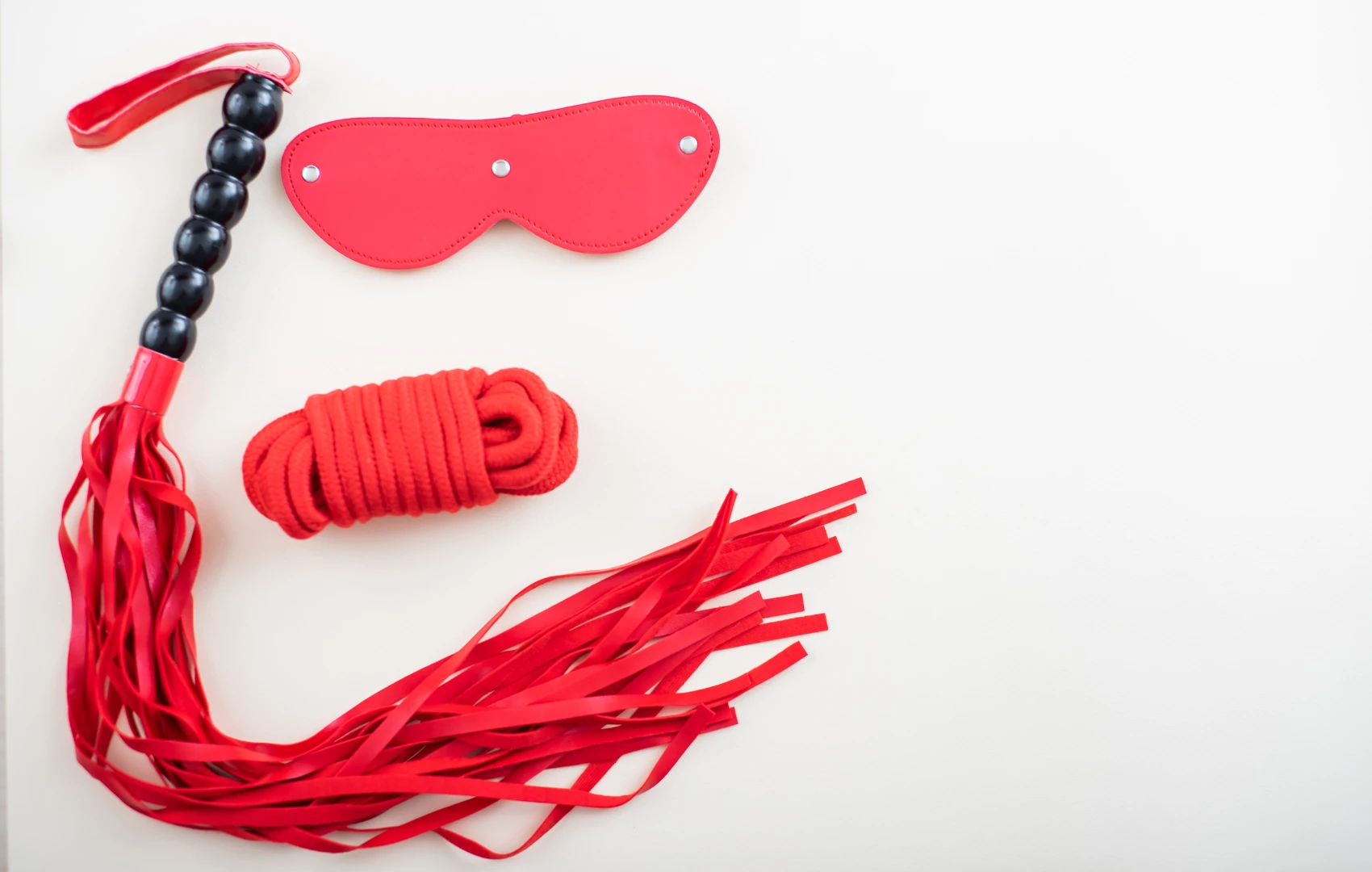 на белом фоне изображен набор БДСМ красного цвета: веревка, маска, плеть