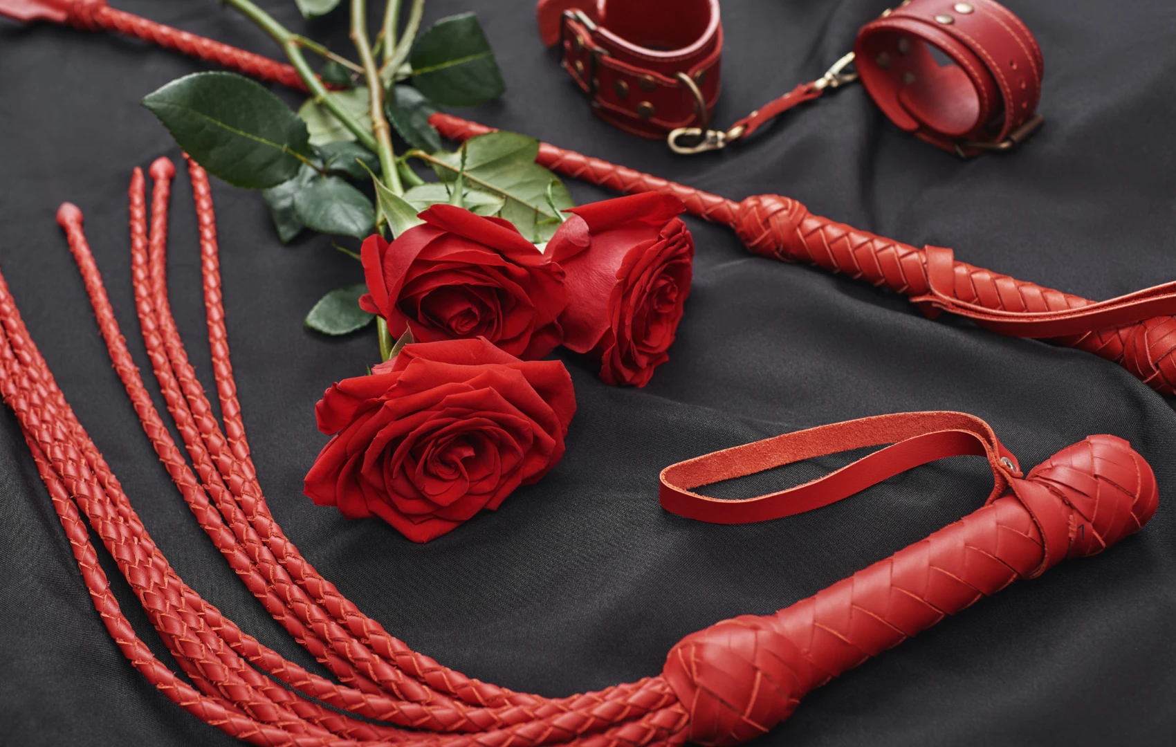 на чорному фоні зображені червоні шкіряні батіг для сексу, стек БДСМ та червоні троянди