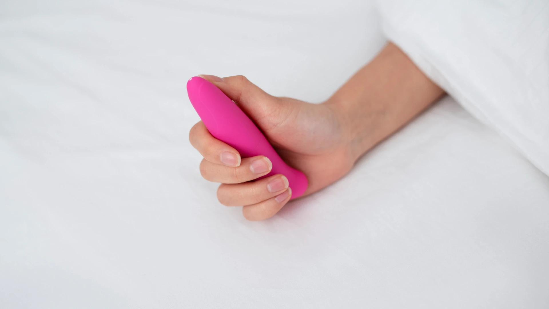 рожевий маленький пальчіковий вібратор в жіночій руці накритою простирадлом білим