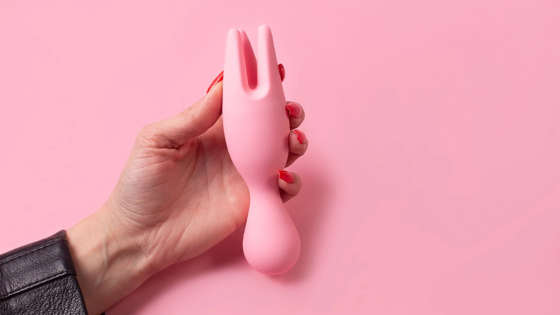 на фото изображен пальчиковый вибратор розовый в женской руке на розовом фоне