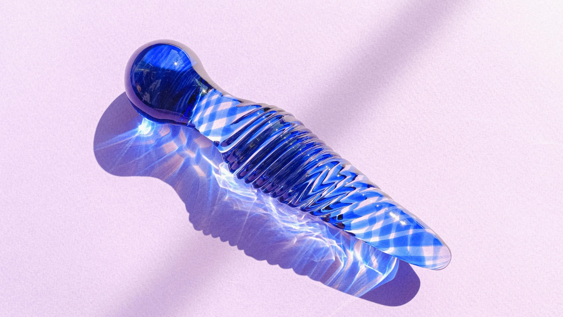 на розовом фоне изображен стеклянный прозрачно-синий дилдо для мастурбации