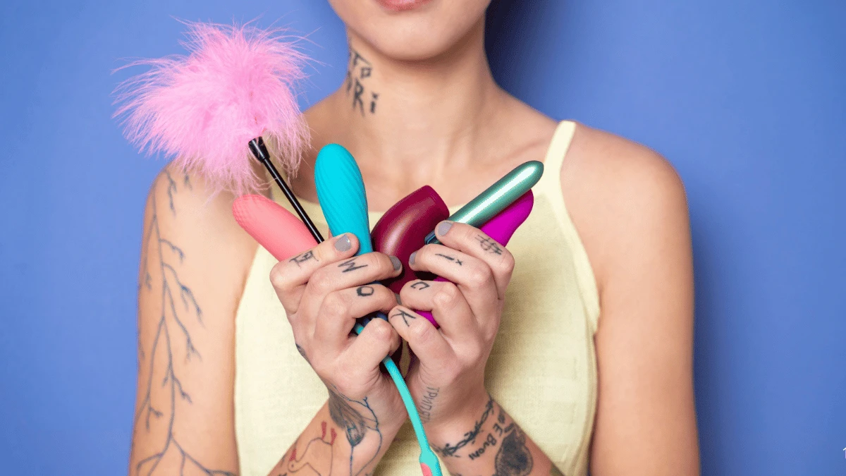 популярні жіночі секс іграшки з сексшоп в руках у жінки з татуюванням на блакитному фоні