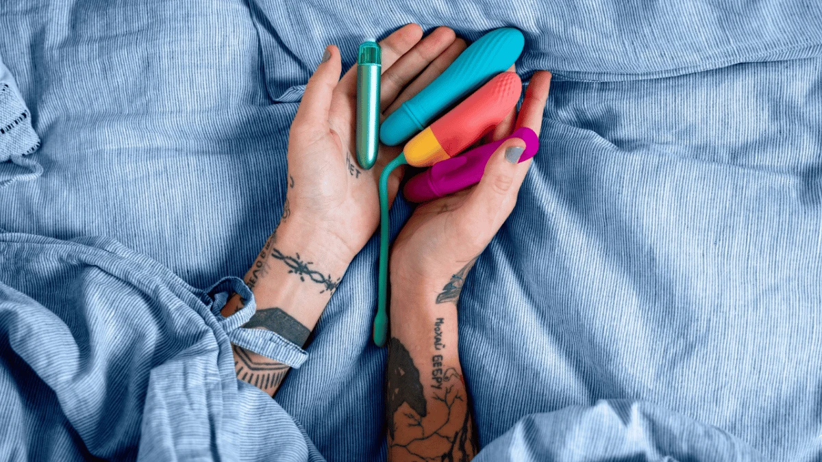 популярні вібратори для жінок та інші секс іграшки в жіночих руках на блакитному простирадлі