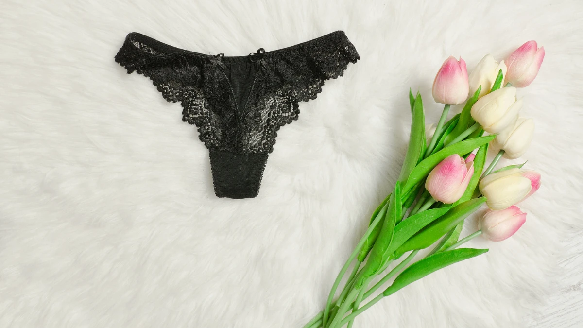 черные эротические кружевные трусы на белом ковре и букет розовых тюльпанов